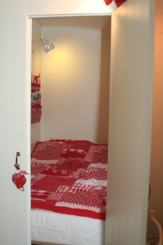 Acogedor rincón para dormir con edredón rojo en Pipowagen, Camping De Grienduil, Países Bajos.