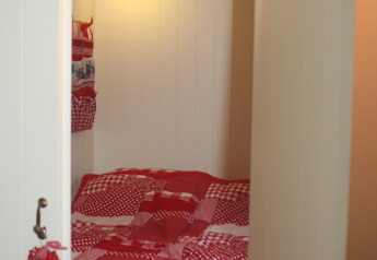 Gemütliche Schlafkoje mit roter Patchwork-Decke in Pipowagen im Camping De Grienduil in den Niederlanden.