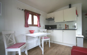 Cuisine lumineuse d’un lodge avec armoires blanches, rideaux à carreaux et table pour deux personnes.