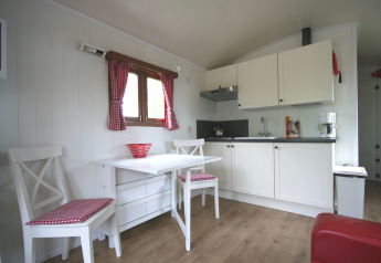 Cuisine lumineuse d’un lodge avec armoires blanches, rideaux à carreaux et table pour deux personnes.