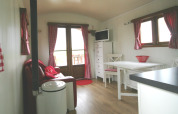 Acogedor interior de la Pipowagen en Camping De Grienduil, Países Bajos, con cortinas rojas y muebles blancos.