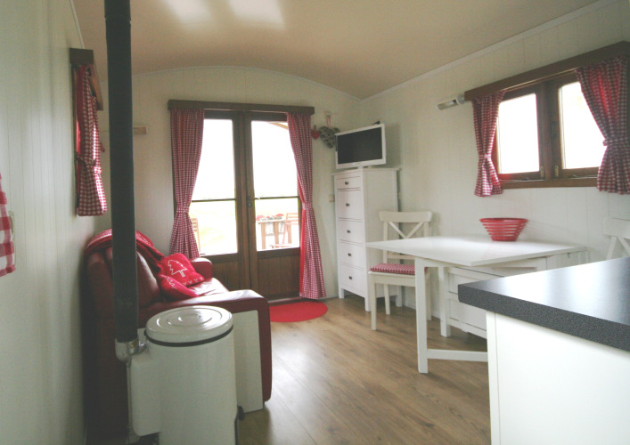 Acogedor interior de la Pipowagen en Camping De Grienduil, Países Bajos, con cortinas rojas y muebles blancos.