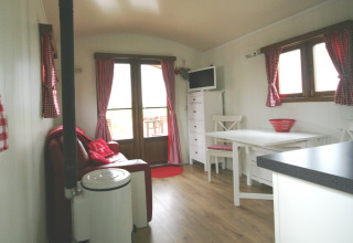 Acogedor interior de la Pipowagen en Camping De Grienduil, Países Bajos, con cortinas rojas y muebles blancos.