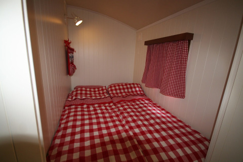 Soveværelse i Pipowagen på Camping De Grienduil, Nederlandene, med rødtternet sengetøj og gardiner.