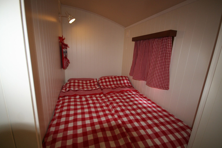 Dormitorio en Pipowagen, Camping De Grienduil, Países Bajos, con ropa de cama y cortinas a cuadros rojos.