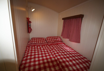 Dormitorio en Pipowagen, Camping De Grienduil, Países Bajos, con ropa de cama y cortinas a cuadros rojos.