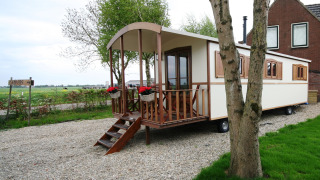 Foto del lodge Pipowagen con veranda in legno, fioriere e vista su un ampio paesaggio verde.