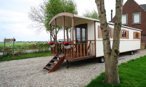 Foto de la casa rodante Pipowagen con porche de madera, cestas de flores y paisaje campestre verde.