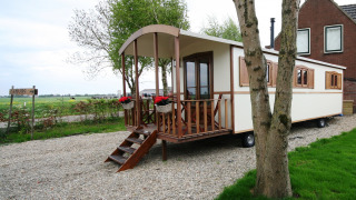 Foto von einer Pipowagen-Lodge mit Holzveranda, Blumen und weitem Blick auf das ländliche Umland.