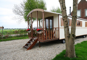 Foto von einer Pipowagen-Lodge mit Holzveranda, Blumen und weitem Blick auf das ländliche Umland.