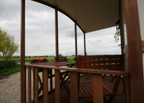 View from a covered wooden porch at Pipowagen, Camping De Grienduil in the Netherlands, overlooking fields.