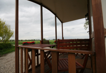 Vista dal portico in legno coperto del Pipowagen al Camping De Grienduil, Paesi Bassi, con campi verdi.