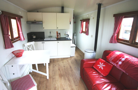 Innenraum der Pipowagen-Lodge auf Camping De Grienduil in den Niederlanden mit rotem Sofa und Küche.