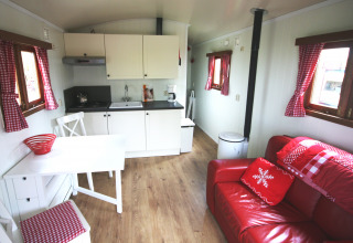 Interior de la cabaña Pipowagen en Camping De Grienduil, Países Bajos, con sofá rojo y cocina acogedora.