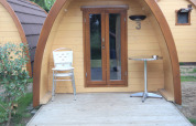 Ingresso della tiny house Pod Traditional con sedie e tavolo sulla terrazza, Camping De Grienduil, Paesi Bassi.