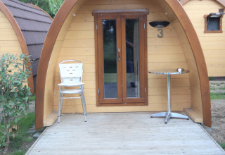 Eingang zu einem kleinen Holzhaus, Pod Traditional, mit Stühlen und Tisch, Camping De Grienduil, Niederlande.
