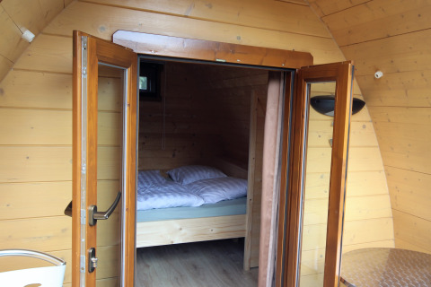 Interior de casa pequeña de madera con puertas de vidrio abiertas y vista a la cama en Pod Traditional, Países Bajos.