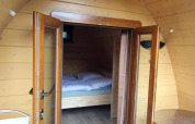 Interior de casa pequeña de madera con puertas de vidrio abiertas y vista a la cama en Pod Traditional, Países Bajos.