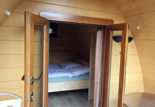 Interior de casa pequeña de madera con puertas de vidrio abiertas y vista a la cama en Pod Traditional, Países Bajos.