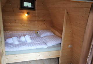 Acogedor dormitorio de madera en la tiny house Pod Traditional con cama doble y sábanas blancas suaves.