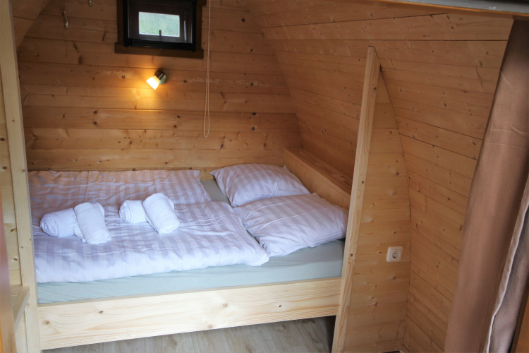 Acogedor dormitorio de madera en la tiny house Pod Traditional con cama doble y sábanas blancas suaves.