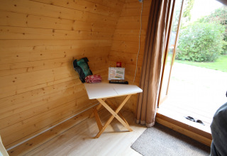 Interior de una pequeña casa de madera con una mesa, objetos encima y puerta abierta al jardín.
