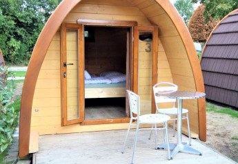 Piccola casa in legno Pod Traditional con porte aperte, terrazza, tavolo e sedie al Camping De Grienduil, Paesi Bassi.