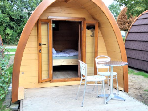 Lille træhytte kaldet Pod Traditional med åbne døre, terrasse, bord og stole i Camping De Grienduil, Holland.
