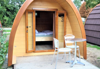 Lille træhytte kaldet Pod Traditional med åbne døre, terrasse, bord og stole i Camping De Grienduil, Holland.