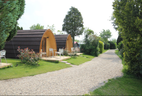 Two cozy Megapod VIP tiny houses with small terrace seating near a gravel path surrounded by greenery.