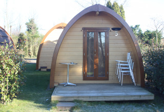 The Megapod VIP tiny house at Camping De Grienduil in the Netherlands, with deck, stacked chairs, and table.