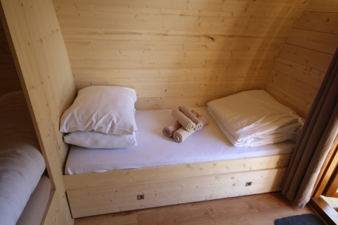 Gemütlicher Schlafbereich mit Holzwänden, Einzelbett, Kissen und Handtüchern in The Megapod VIP, Niederlande.