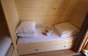 Knusse houten slaapruimte met eenpersoonsbed, kussens en handdoeken in The Megapod VIP in Nederland.