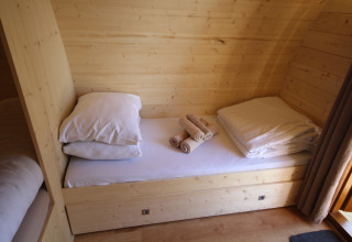 Acogedora zona de dormitorio de madera con cama individual, almohadas y toallas en The Megapod VIP en Holanda.