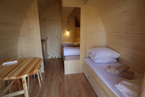 Vista interior de la tiny house The Megapod VIP con paredes de madera, camas y mesa en los Países Bajos.