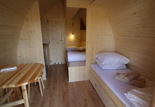 Vista interior de la tiny house The Megapod VIP con paredes de madera, camas y mesa en los Países Bajos.