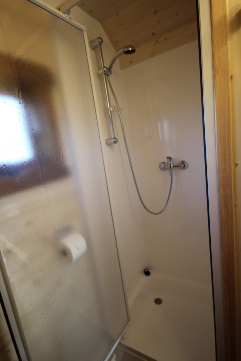Kleine douchecabine met glazen schuifdeur en wc-rolhouder in The Megapod VIP, Camping De Grienduil.
