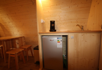 Piccolo angolo cottura nel Megapod VIP con pareti in legno, tavolo, sedie, macchina da caffè e mini frigo.