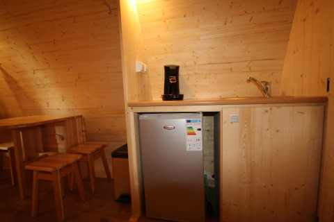 Kleine kitchenette in The Megapod VIP met houten wanden, tafel, stoelen, koffiemachine, minibar en gootsteen.