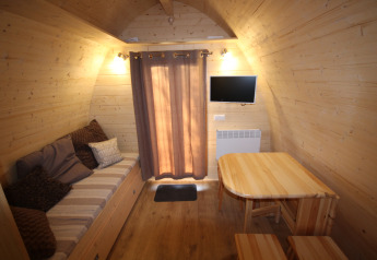 Interiør af et lille træhus med sofa, bord, stole, TV og gardiner, Megapod VIP, Camping De Grienduil.