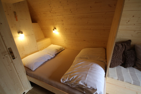 Knusse slaapkamer met tweepersoonsbed en houten muren in The Megapod VIP bij Camping De Grienduil, Nederland.