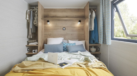 Modernes, gemütliches Schlafzimmer in einem Tiny House mit offenem Fenster, hellen Kissen und Holzdesign.