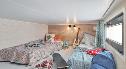 Dormitorio en Tiny House 11 en Camping De Grienduil, Países Bajos, con dos camas, guitarra y monopatín.