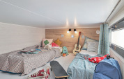 Dormitorio en Tiny House 11 en Camping De Grienduil, Países Bajos, con dos camas, guitarra y monopatín.