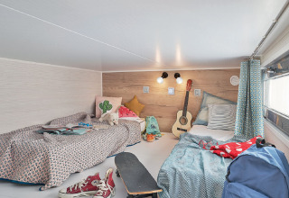 Dormitorio en Tiny House 11 en Camping De Grienduil, Países Bajos, con dos camas, guitarra y monopatín.