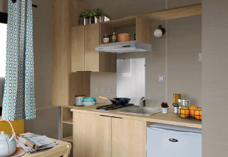 Kompakte Küche im Tiny House 11 von Camping De Grienduil, Niederlande, mit Holzschränken und Mini-Kühlschrank.
