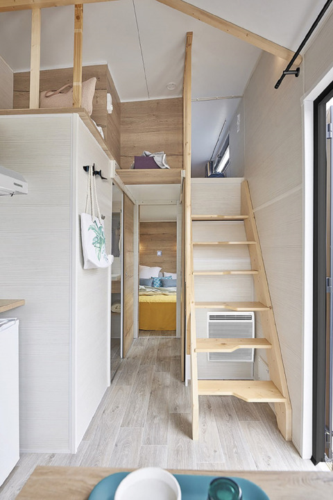Innenraum eines Tiny House mit Mezzanin, Holztreppe und Schlafzimmer bei Camping De Grienduil, Niederlande.
