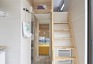 Innenraum eines Tiny House mit Mezzanin, Holztreppe und Schlafzimmer bei Camping De Grienduil, Niederlande.