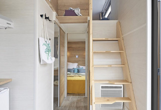 Interieur van een tiny house met een mezzanine, houten trap en slaapkamer bij Camping De Grienduil.