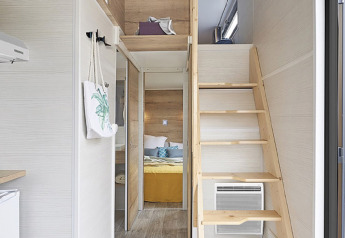 Intérieur d'une tiny house avec mezzanine, escalier en bois et chambre au Camping De Grienduil, Pays-Bas.